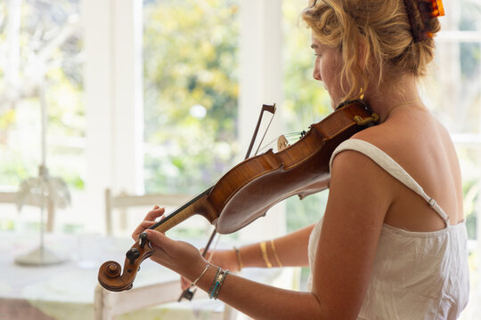 young woman musician playing her violin in light filled room