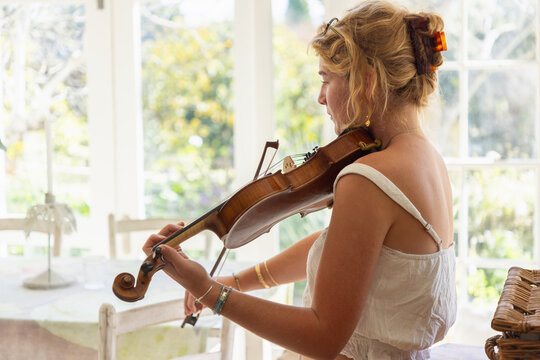 young woman musician playing her violin in light filled room