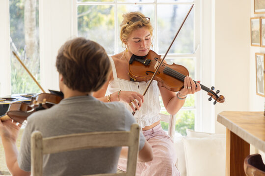 young woman musician playing her violin in light filled room