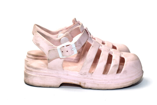 A side view of a worn pair of light pink kids jelly sandals with buckles, isolated on a white background.