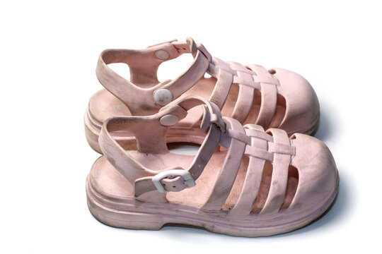 A pair of dirty, light pink rubber jelly sandals for kids, placed on a white surface.