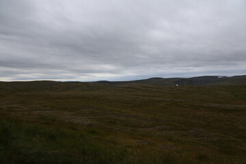 Rolling arctic mountain tundra with scattered patches of snow under an overcast grey sky near Nordkapp, Norway. © Adam