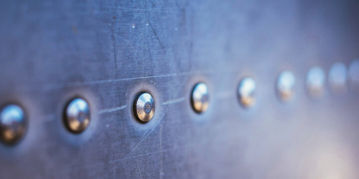 Brushed blue metal surface with row of rivets signifies industrial strength and engineering technology.