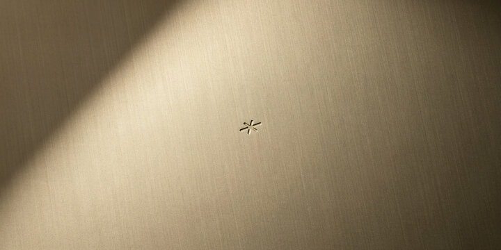 Brushed gold metal surface with minimal asterisk symbol and diagonal shadow.