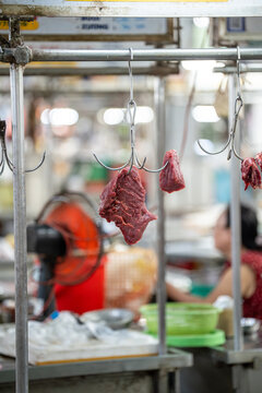 Raw beef or pork meat hanging on metal hooks selling at street food market stall, fresh meat wholesale, Asian wet market selling fresh produce and various ingredients for customers on daily basis.