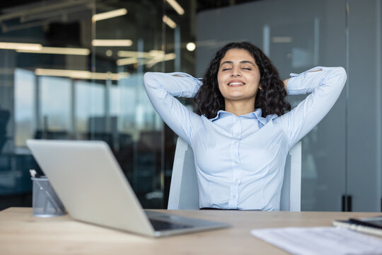 Young businesswoman leaning back in her office chair with arms behind head, smiling with closed eyes, finding relief and satisfaction after completing a task in a contemporary workspace