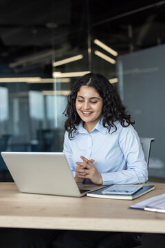 Young professional woman engaging in an online video call on a laptop, actively participating in a virtual meeting or remote collaboration while working at her modern office desk