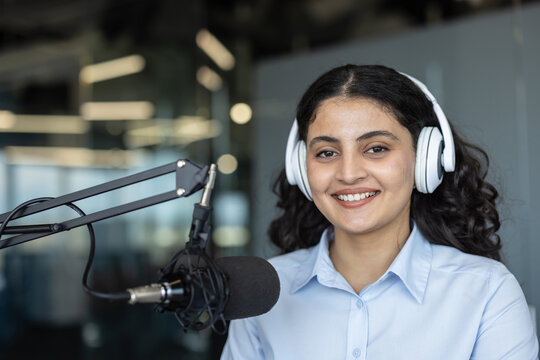 Young indian woman smiling and wearing headphones, actively recording or hosting a podcast with a professional microphone in a modern broadcasting studio, communicating and sharing ideas