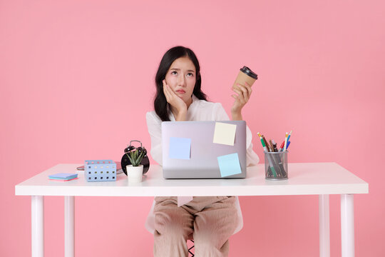 Tired asian businesswoman holding coffee beside laptop expressing work burnout mental fatigue low motivation deadline stress productivity pressure and need for work life balance.