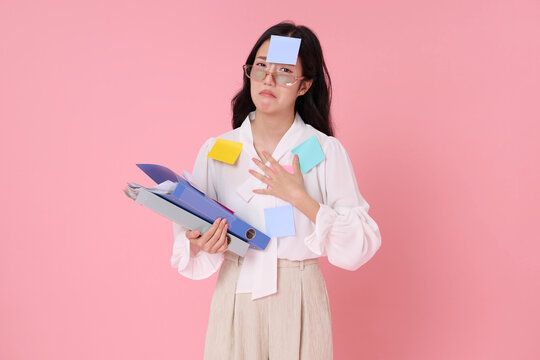 Overwhelmed businesswoman holding office folders with sticky notes expressing workload stress burnout risk deadline pressure fatigue multitasking strain and need for work life balance.
