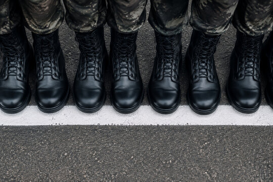 A top-down view of a row of identical black boots aligned on a white line.