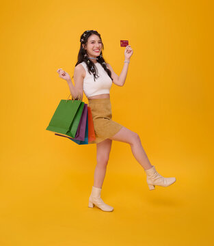 Young woman holding credit card and shopping bags while walking expressing retail shopping cashless payment consumer confidence purchasing power financial freedom and joyful modern lifestyle.