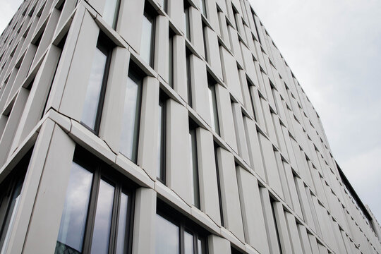 Modern industrial white office building exterior facade with the background of a grey moody sky. White panels, big reflective windows, geometric design.Urban architecture , property element detail