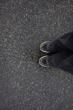 Feet of woman in sneakers and loose grey jeans standing on wet asphalt after the rain close up top view. Human in the city, walk in rainy weather, minimalistic background