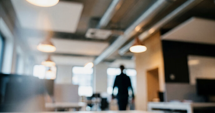 A blurred image of a man walking in a modern office space, showcasing contemporary workplace design and lighting in an ambiguous, atmospheric setting.