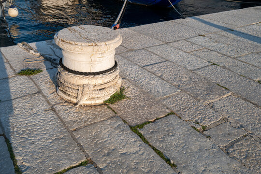 Close-up of old stone bollard by water, with dock tiles and sunlight