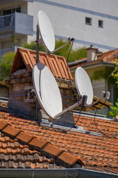 White satellite dishes installed on a tiled rooftop of a residential building