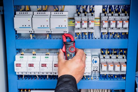 Electrician hand holding a clamp meter while checking electrical panel and circuit breakers with electrician