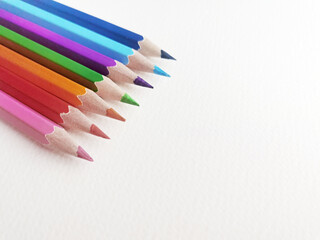 Fototapeta premium Colored pencils lined at angle on white textured paper surface