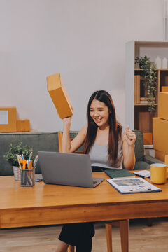 Startup SME small business entrepreneur of freelance Asian woman wearing apron using laptop and box to receive and review orders online to prepare to pack sell to customers, online sme business ideas.