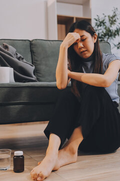 Young Asian woman sitting in bed and holding her head in pain with headache, feeling depressed 

and suffering