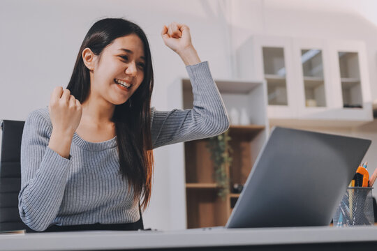Young asian businesswoman is smiling and working on a laptop while sitting at her desk in a modern office