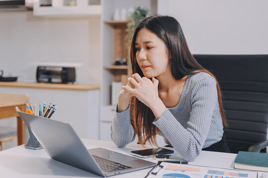Young Asian woman sits at office desk rubbings her eyes and temples feeling pain. Stress. And exhaustion from long hours working on the computer