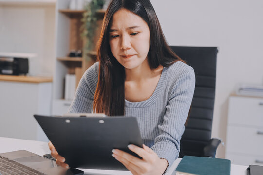 Young Asian woman sits at office desk rubbings her eyes and temples feeling pain. Stress. And exhaustion from long hours working on the computer