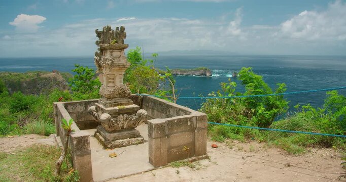 Traditional stone shrine overlooks tropical islands and blue sea from cliff top in Nusa Penida