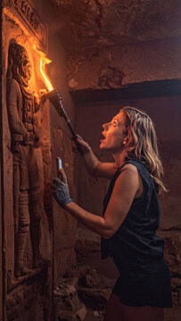 A brave female archaeologist holds a burning torch, discovering an ancient stone carving inside a dark, mysterious tomb. Evoking wonder and suspense, ideal for adventure concepts.