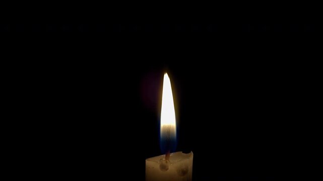 White paraffin candle with yellow tints burns on a black background. White paraffin candle flame burning on black background. Slow Motion. 4K Video
