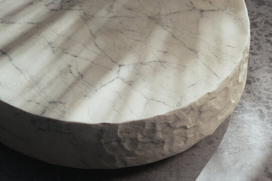 Minimalist 3D render of round beige marble table with a rough raw edge on a concrete floor in soft natural sunlight. Empty display stage with botanical window gobo shadow and copy space for cosmetics.