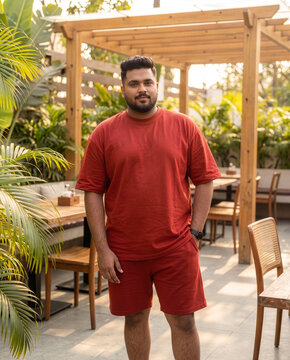 Plus size Indian man in rust red oversized t-shirt and matching shorts standing in outdoor cafe patio Generative Ai