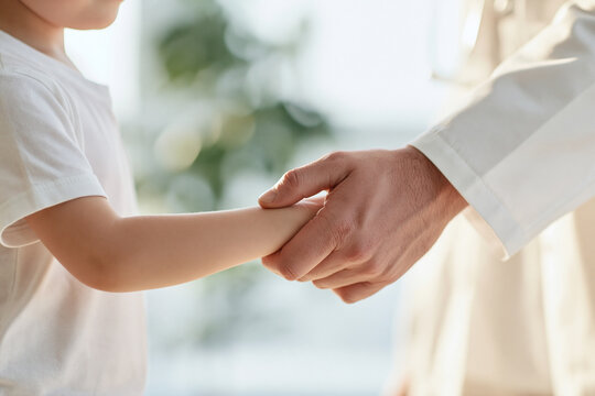 Doctor gently holds child's arm, showing care and trust in a clinic. Medical partnership concept for healthcare.