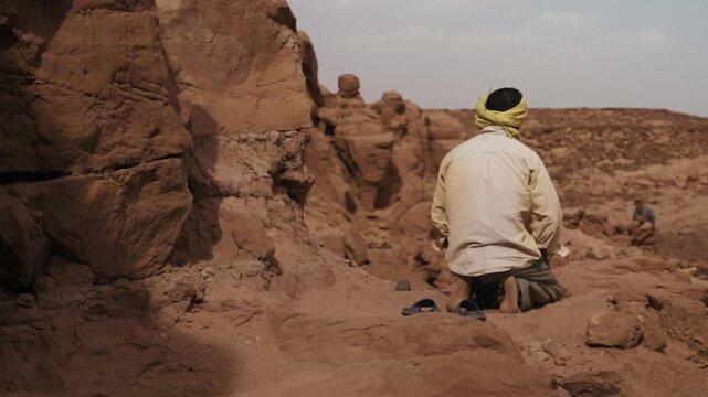 Religious man performing the traditional Islamic prayer ritual in a rocky desert landscape