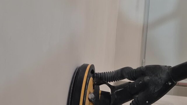 Slow motion footage along the wall of a drywall sander machine moving up and down sanding the painted wall surface.