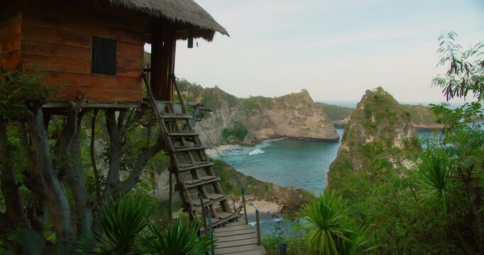 Small wooden hut built into trees features rustic ladder facing beautiful bay and rocky islands in Nusa Penida