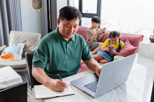 Father working remotely while children use mobile devices.