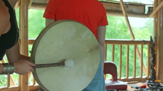 The hands of a girl playing a shamanic drum with the wooden stick.