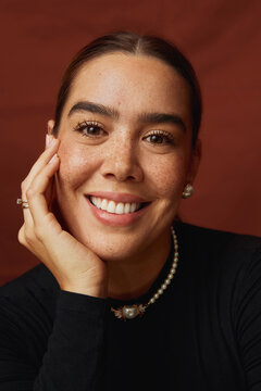 Smiling woman with pearls and a dark blouse on a red background.