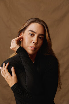 Woman with long hair wearing a black sweater on a brown background