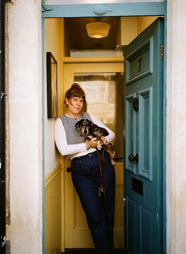 Woman Stands at Door Holding a Dog in Her Arms
