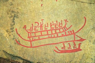 Tanumshede, Sweden - 09.06.2026: Ancient Bronze Age rock carvings of stylized ships with human figures painted in red pigment on textured stone © Andrei