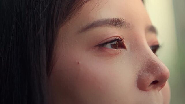 Close up of young Asian woman slowly opening her eyes with natural skin and calm expression, beauty face detail focusing on eyes, eyelashes and skincare in soft light, wellness and self care concept