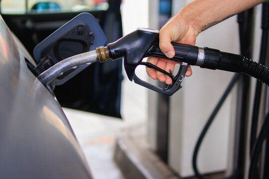 Person refueling a vehicle with a gas pump at an outdoor petrol station, representing current fuel prices, automotive travel, and the economic impact of oil