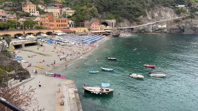 4K video looking east over the coastline of Monterosso al Mare in Cinque Terre, Italy, featuring the beach, colorful waterfront buildings, small boats, clear Ligurian Sea, and rugged Mediterranean coa