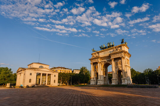 Arco della Pace monument in Milan, Italy, surrounded by green trees and a clear blue sky during golden hour lighting