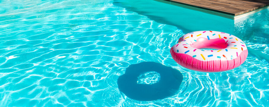 Pink donut inflatable float in turquoise swimming pool with shadow and wooden deck