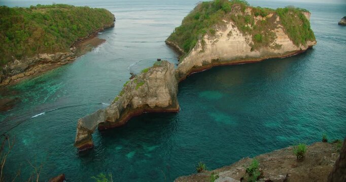 Limestone rock formations rise from turquoise sea near rugged island coast in Nusa Penida Island Bali