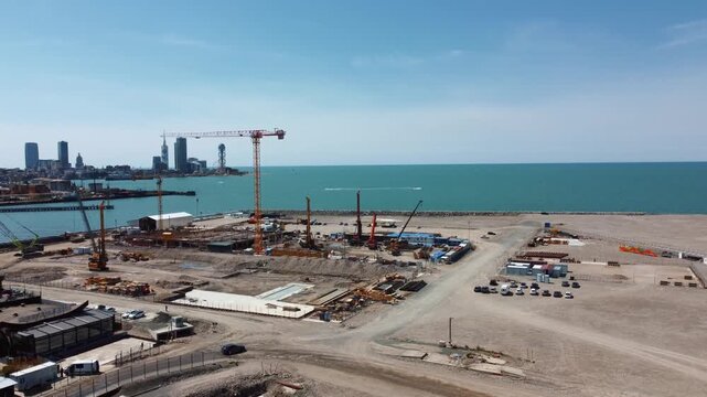 Drone footage orbiting a large construction site on the Black Sea coast shows the first stages of construction of the foundations of an island with heavy machinery against the backdrop of the modern s